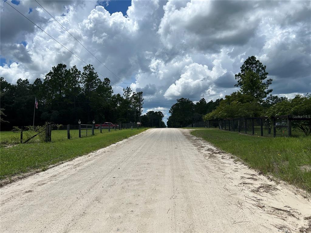 A dirt road stretches between grassy fields lined with wooden fences and trees under a cloudy sky — 0000 SE 25TH STREET, MORRISTON, FL
