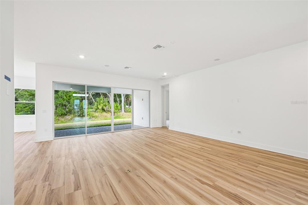 An empty living room features light wood-look flooring, white walls, and large sliding glass doors — 12231 WHITE BLOSSOM COURT, PARRISH, FL