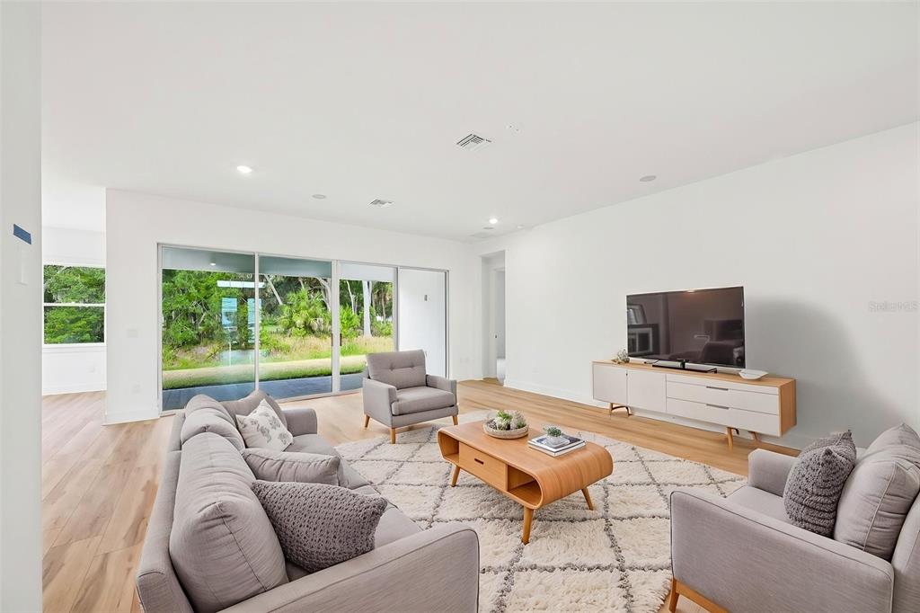 A modern living room features light wood floors, gray furniture, and large sliding glass doors — 12231 WHITE BLOSSOM COURT, PARRISH, FL