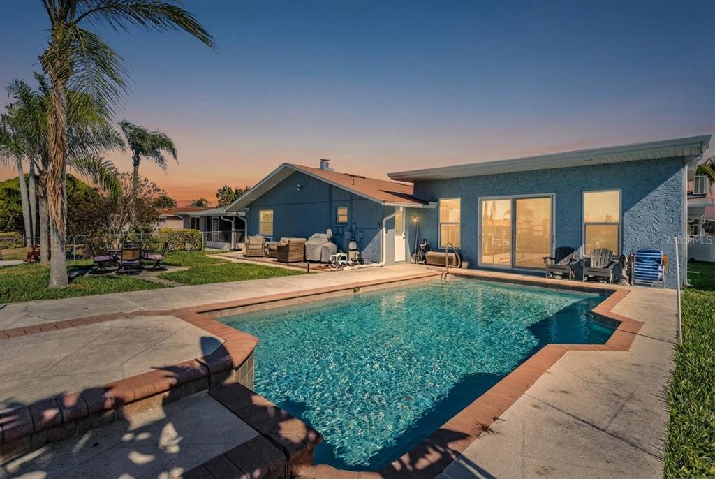 A light blue single-story house features a stone facade, metal roof, and circular driveway — 5001 MARLIN DRIVE, NEW PORT RICHEY, FL