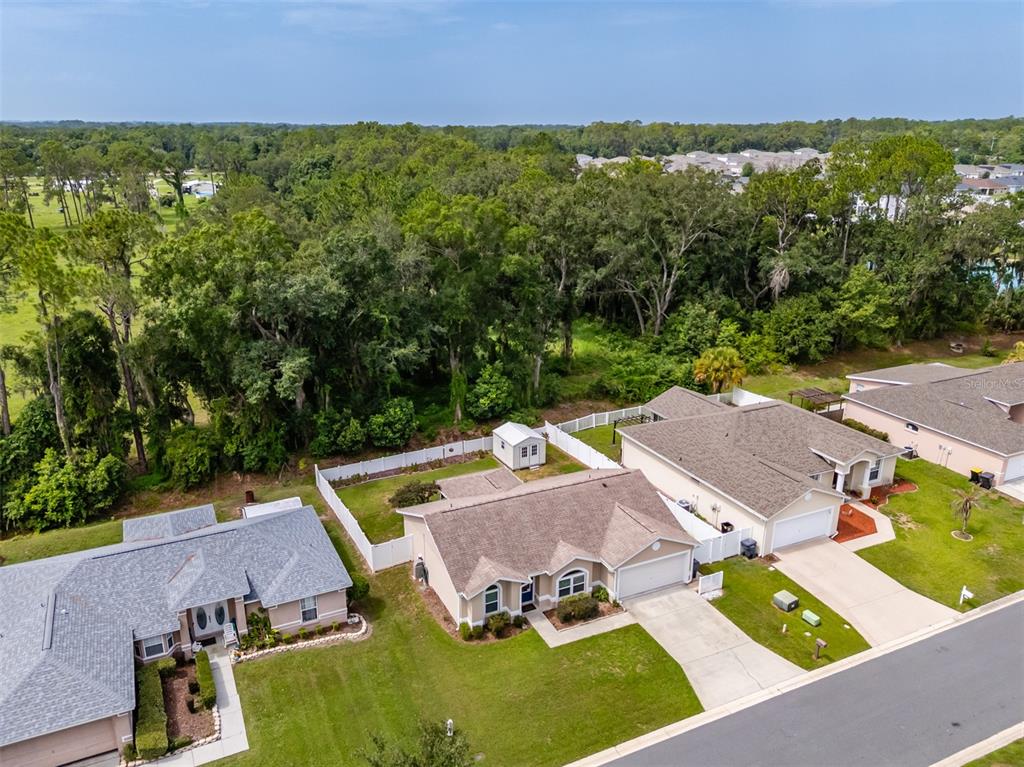 An aerial view shows three suburban houses with driveways and backyards bordering a wooded area — 1746 GREY FOX DRIVE, LAKELAND, FL