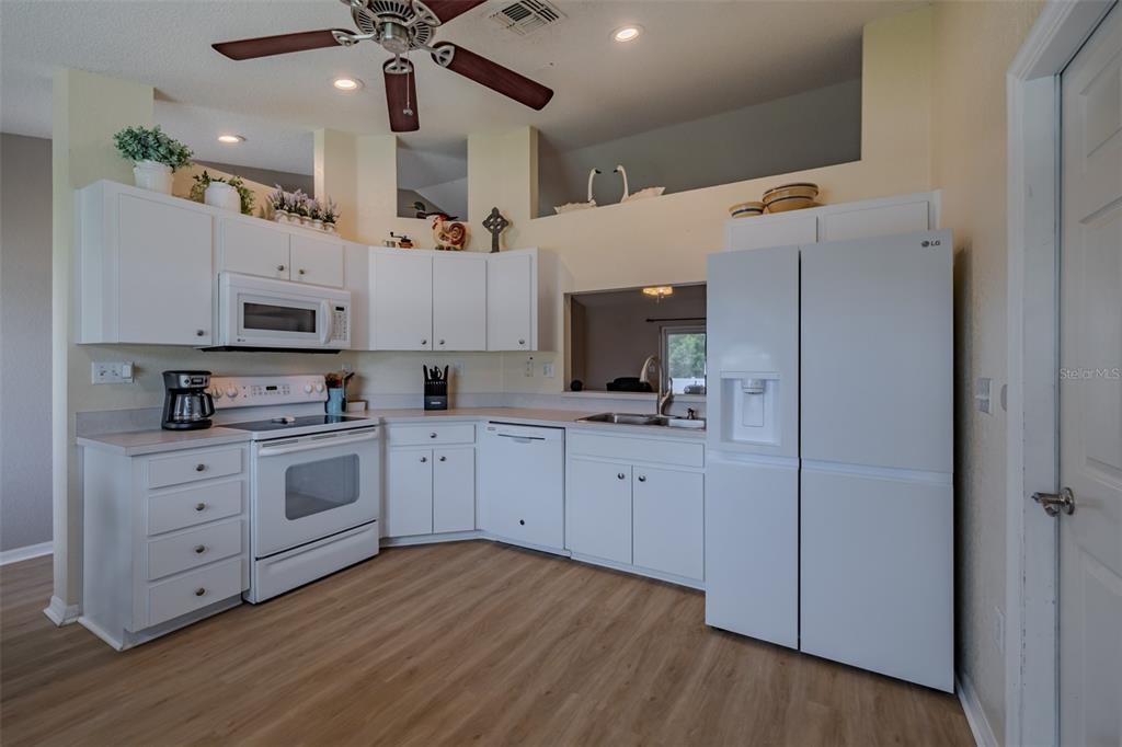 A kitchen features white cabinetry, white appliances, light wood-look flooring, and a ceiling fan — 1746 GREY FOX DRIVE, LAKELAND, FL