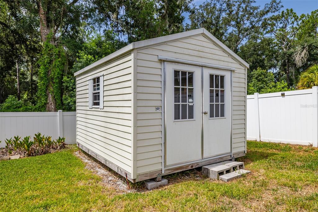 A light-colored vinyl storage shed with double doors sits on a grassy lawn — 1746 GREY FOX DRIVE, LAKELAND, FL