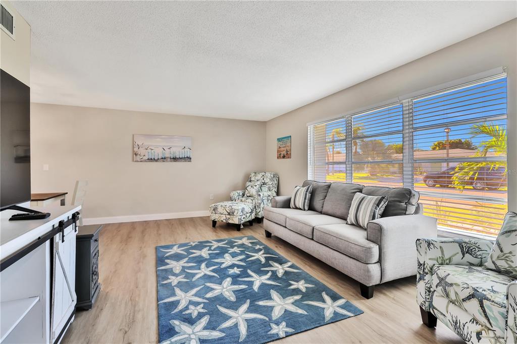 A living room features a grey sofa, patterned armchairs, a starfish rug, and large windows — 6462 OTIS ROAD, NORTH PORT, FL
