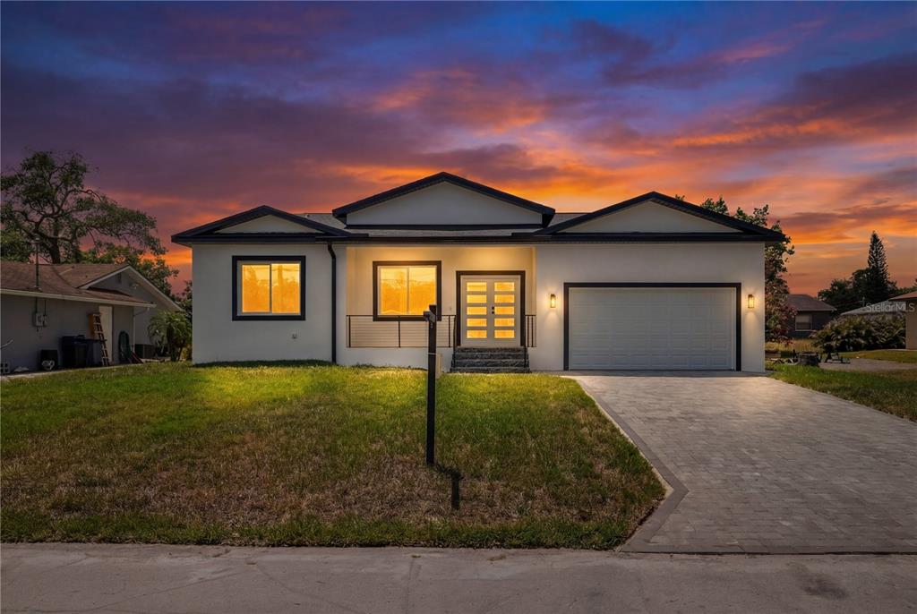 A single-story house with a white exterior, dark trim, and a paved driveway at sunset — 8526 INDIES DRIVE, HUDSON, FL