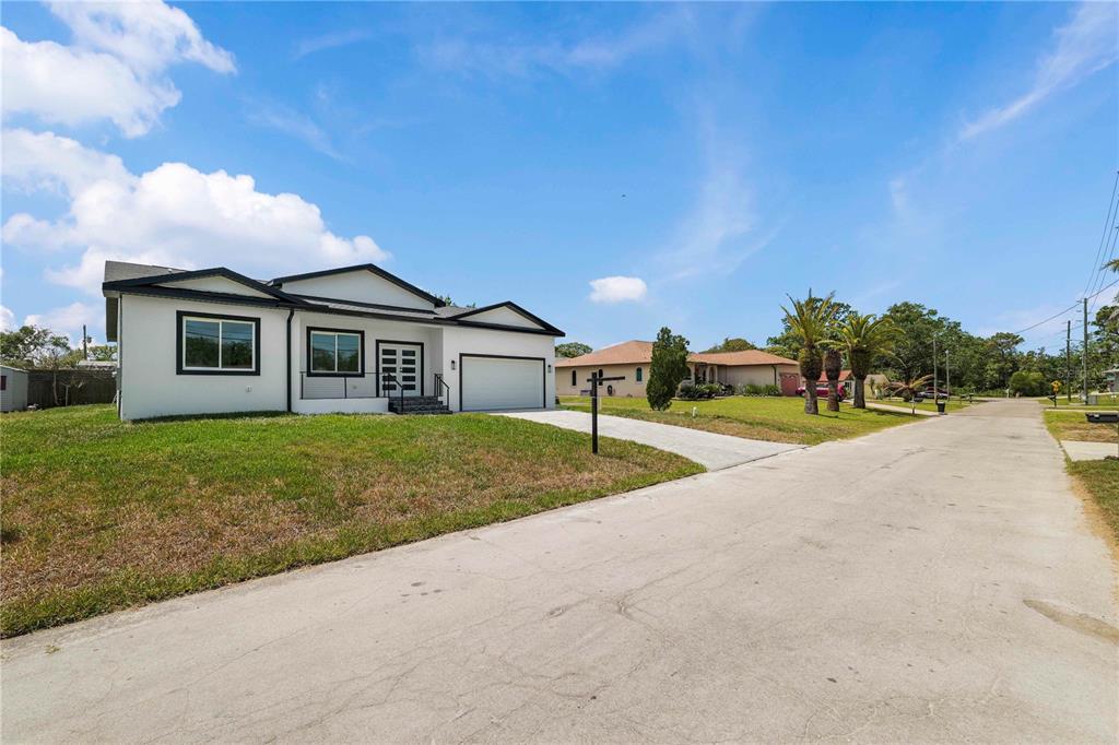 A white single-story house with a black roof and a two-car garage sits on a street — 8526 INDIES DRIVE, HUDSON, FL