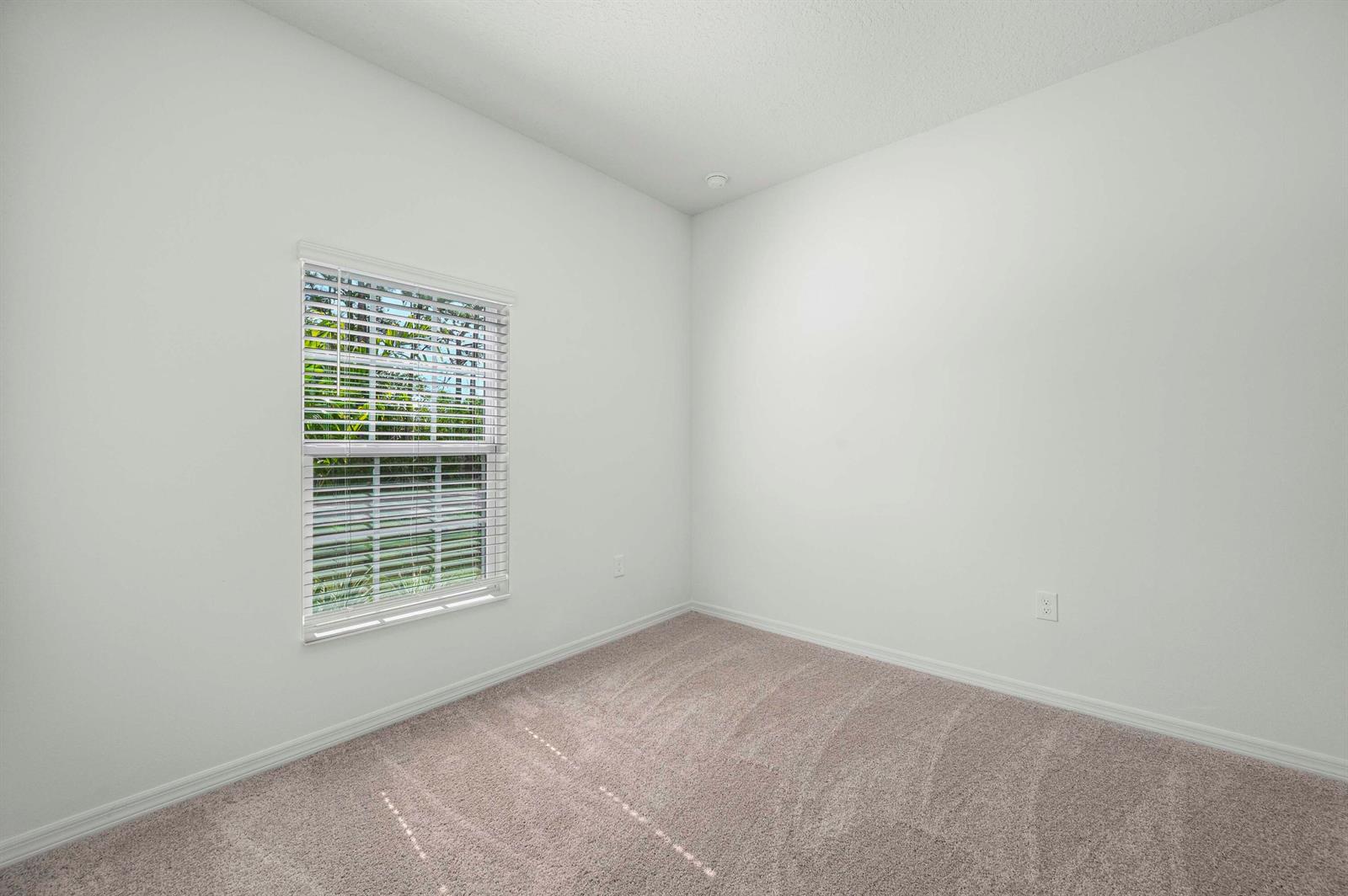 An empty bedroom features white walls, beige carpet, and a window with white blinds — 7885 103rd Court, Vero Beach FL 32967, VERO BEACH, FL
