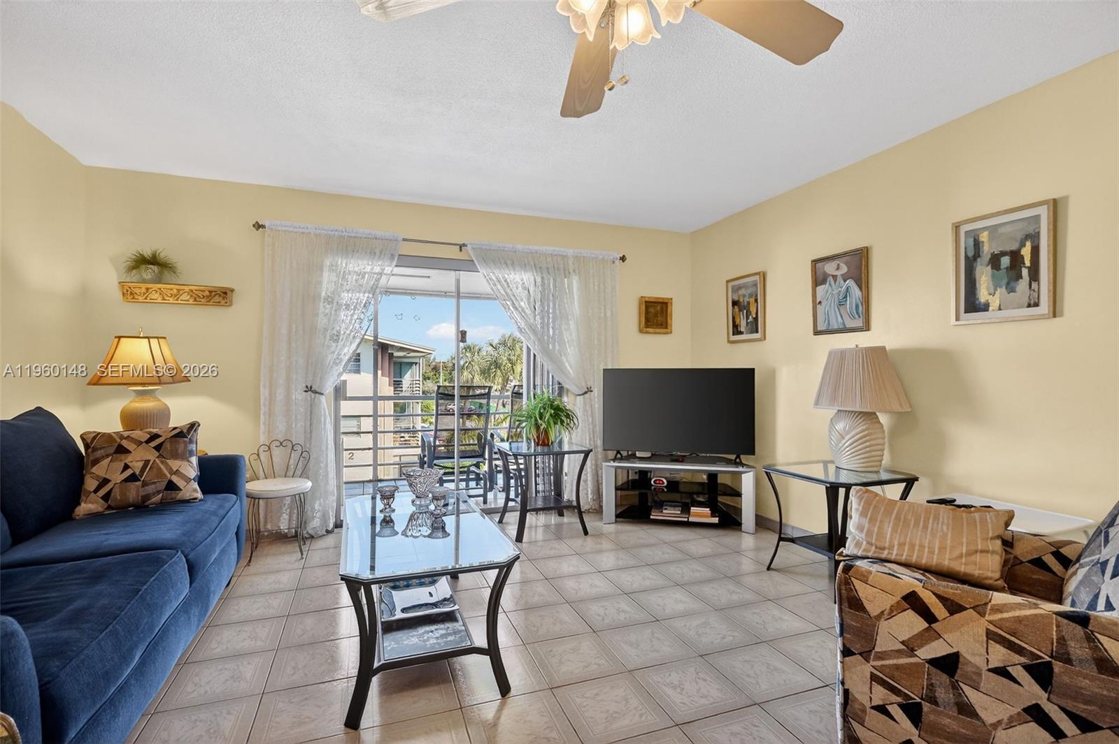 A living room features tile flooring, a blue sofa, a television, and a balcony view — 16900 NE 14th Ave # 302, Miami FL 33162, MIAMI, FL