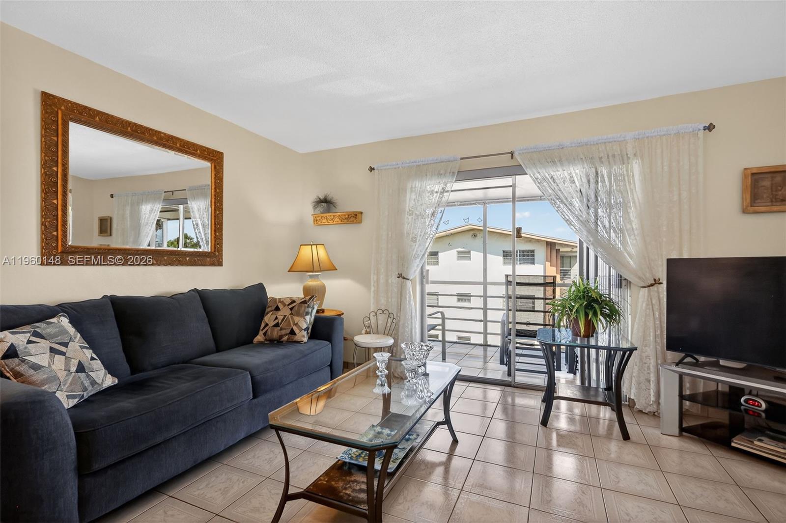 A living room features a dark sofa, glass coffee table, tile flooring, and a balcony view — 16900 NE 14th Ave # 302, Miami FL 33162, MIAMI, FL