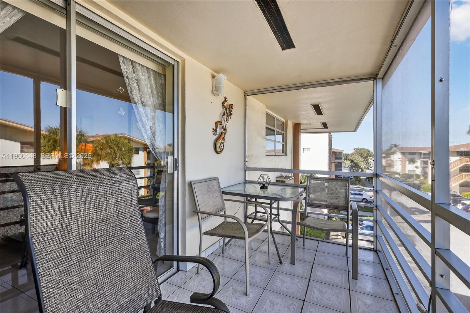 A screened-in balcony features tiled flooring, a small glass table, and three chairs — 16900 NE 14th Ave # 302, Miami FL 33162, MIAMI, FL