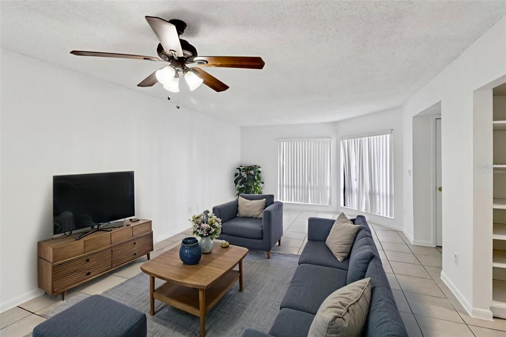 A living room features a blue sofa, matching armchair, wood coffee table, and ceiling fan — 4369 AQUA VISTA DRIVE UNIT 16-C, ORLANDO, FL