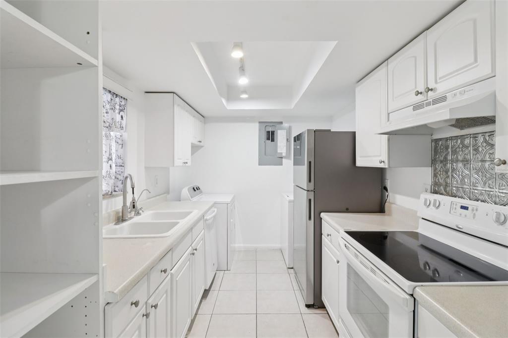 A galley kitchen features white cabinets, tile flooring, a stainless steel refrigerator, and white appliances — 4369 AQUA VISTA DRIVE UNIT 16-C, ORLANDO, FL