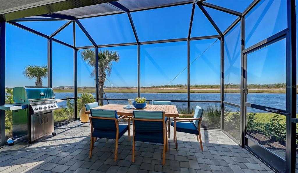 A screened-in patio features a dining set, a grill, and a view of a lake — 2118 SYLVESTER PALM LANE, BRADENTON, FL