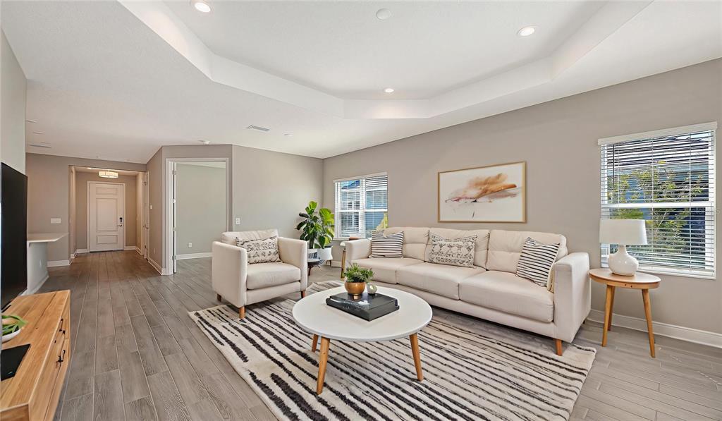A living room with a tray ceiling, light-colored sofa, armchair, and wood-look tile flooring — 2118 SYLVESTER PALM LANE, BRADENTON, FL