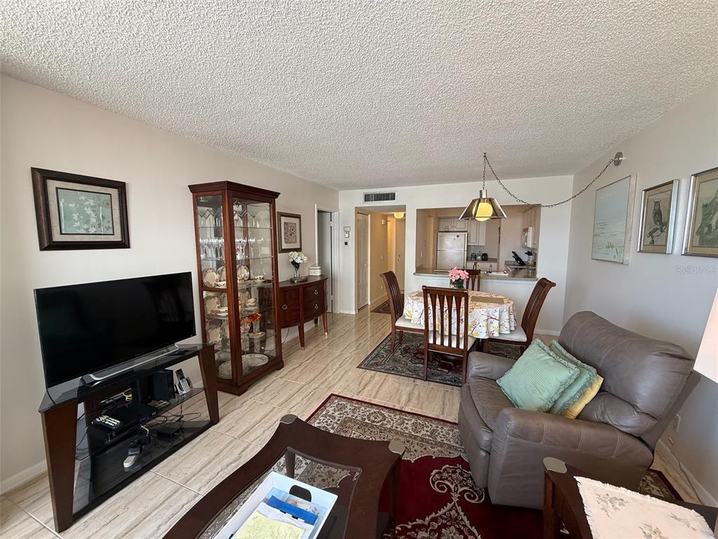 A living and dining area with tile floors, a glass display cabinet, and a television — 6279 SUN BOULEVARD UNIT 403, ST PETERSBURG, FL