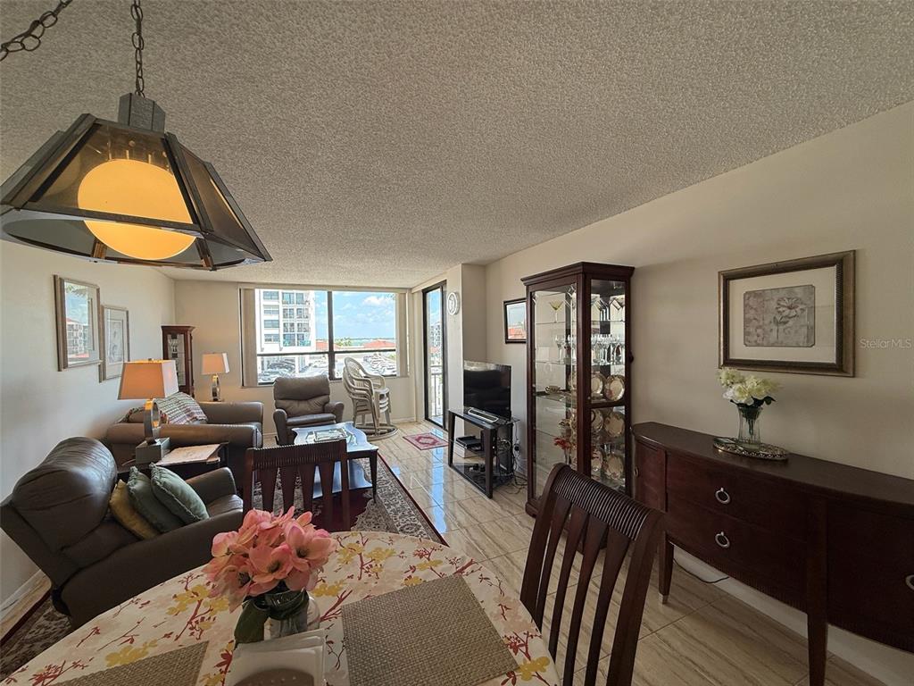 A dining area and living room feature tile flooring, a glass display cabinet, and balcony access — 6279 SUN BOULEVARD UNIT 403, ST PETERSBURG, FL