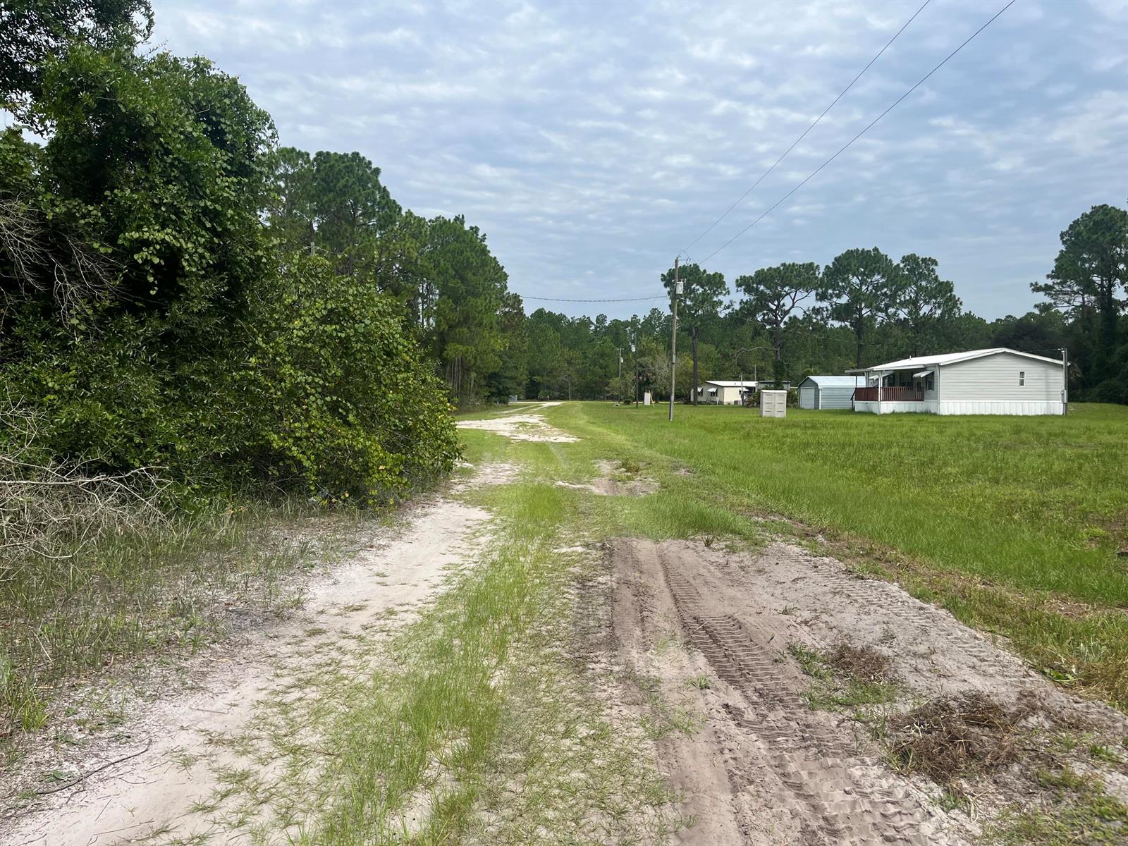 A dirt road leads past a grassy field toward a white manufactured home — 122 Glenside Street, FL 32139, FL