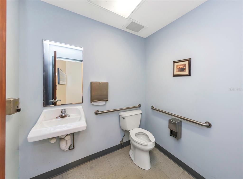 A small, light blue accessible restroom featuring a wall-mounted sink, toilet, and grab bars — 2346 DREW STREET UNIT 1F, CLEARWATER, FL