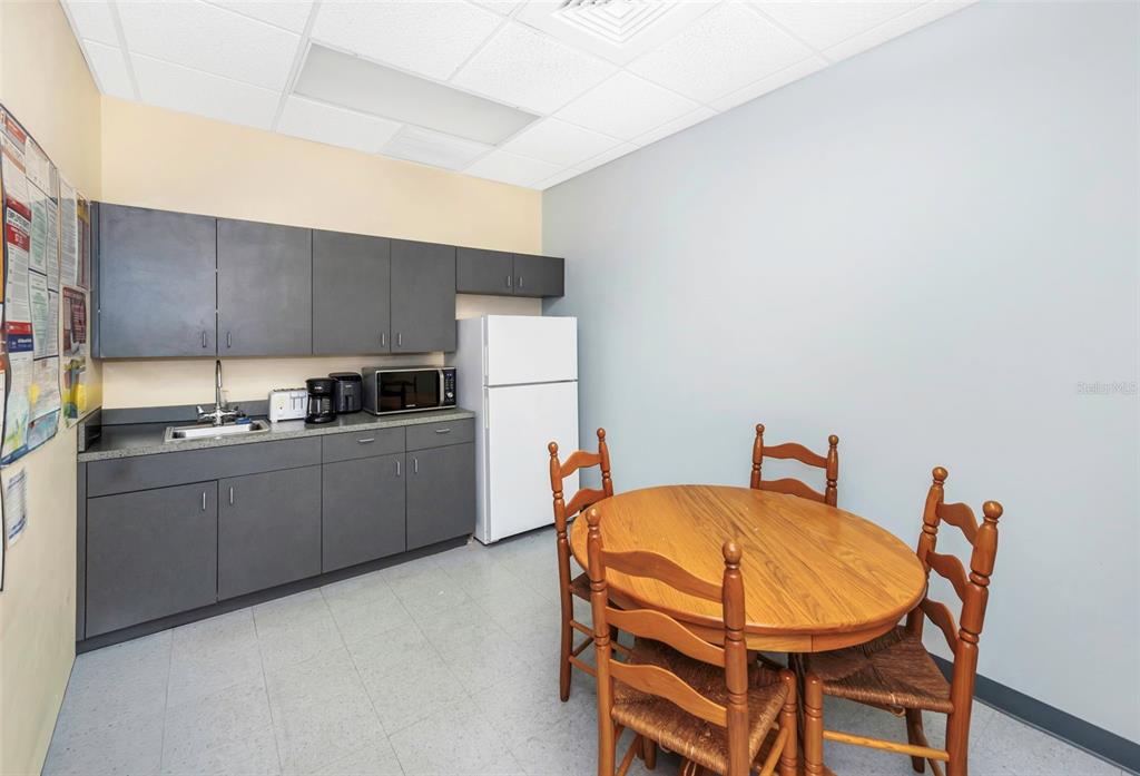 A breakroom features gray cabinetry, a white refrigerator, a sink, and a wooden dining set — 2346 DREW STREET UNIT 1F, CLEARWATER, FL