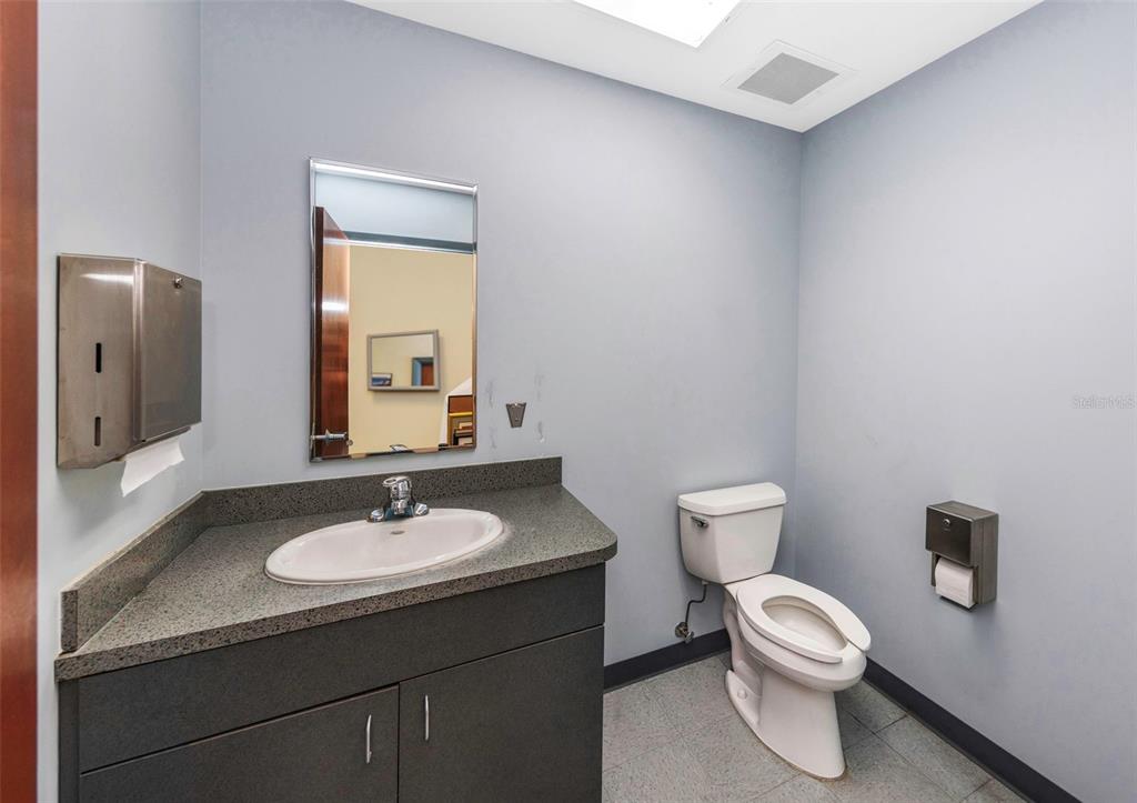 A small bathroom features a gray vanity with a sink, a mirror, and a toilet — 2346 DREW STREET UNIT 1F, CLEARWATER, FL