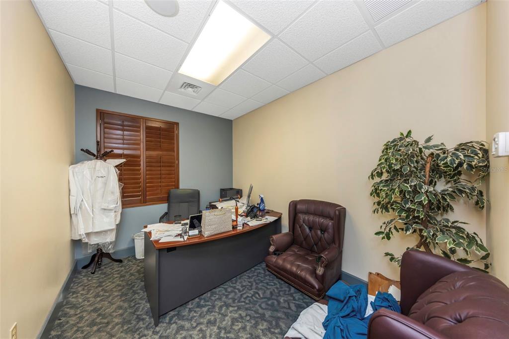 An office features a desk, two leather chairs, a potted plant, and a window with shutters — 2346 DREW STREET UNIT 1F, CLEARWATER, FL