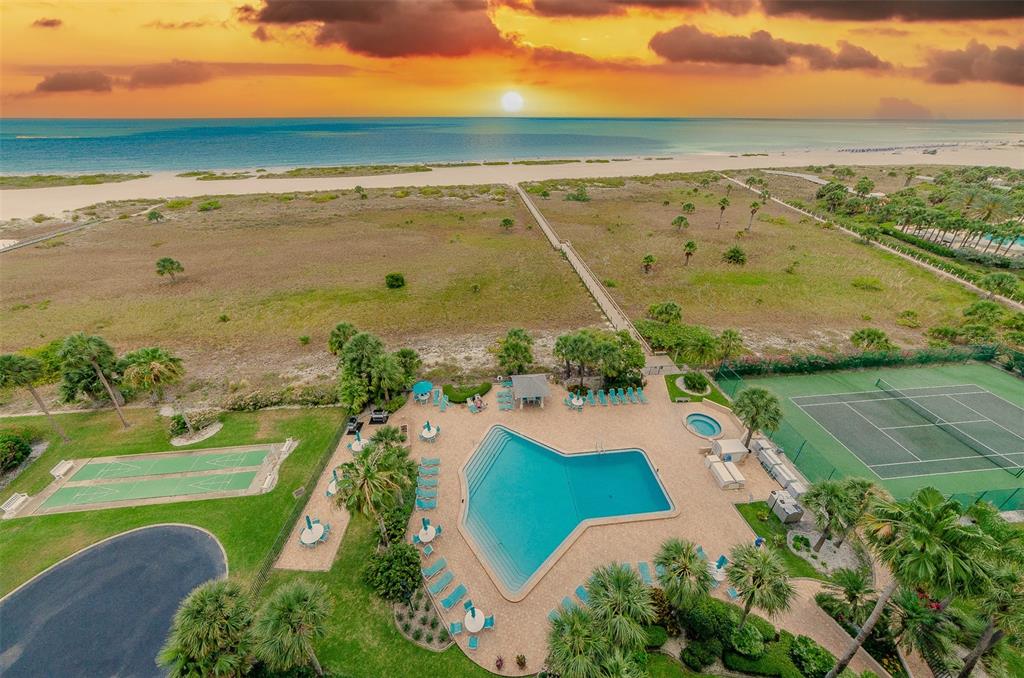 An aerial view shows a swimming pool, tennis court, and boardwalk leading to a beach — 1230 GULF BOULEVARD UNIT 1404, CLEARWATER, FL