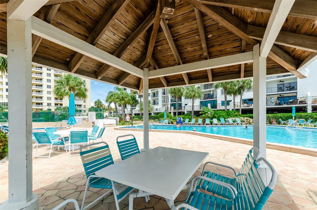 A covered patio with a table and chairs overlooks a swimming pool and apartment buildings — 1230 GULF BOULEVARD UNIT 1404, CLEARWATER, FL
