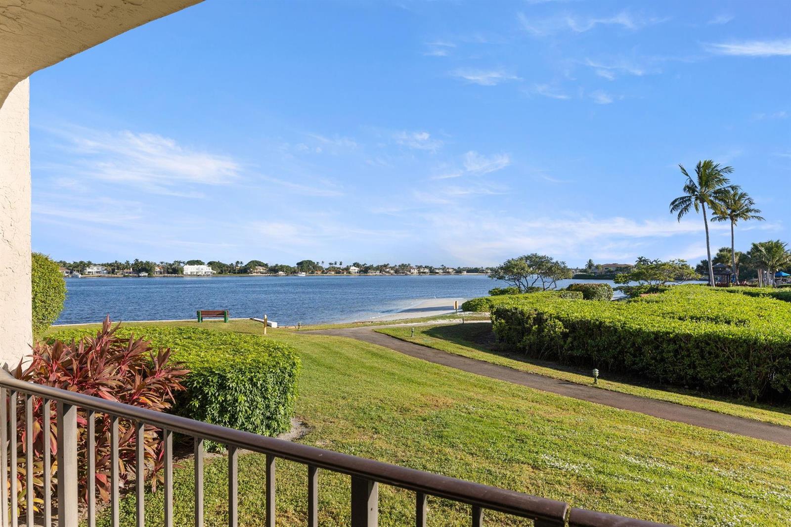 A balcony view overlooks a grassy lawn, a paved path, and a wide waterfront area — 7020 Half Moon Circle # 105, Hypoluxo FL 33462, HYPOLUXO, FL