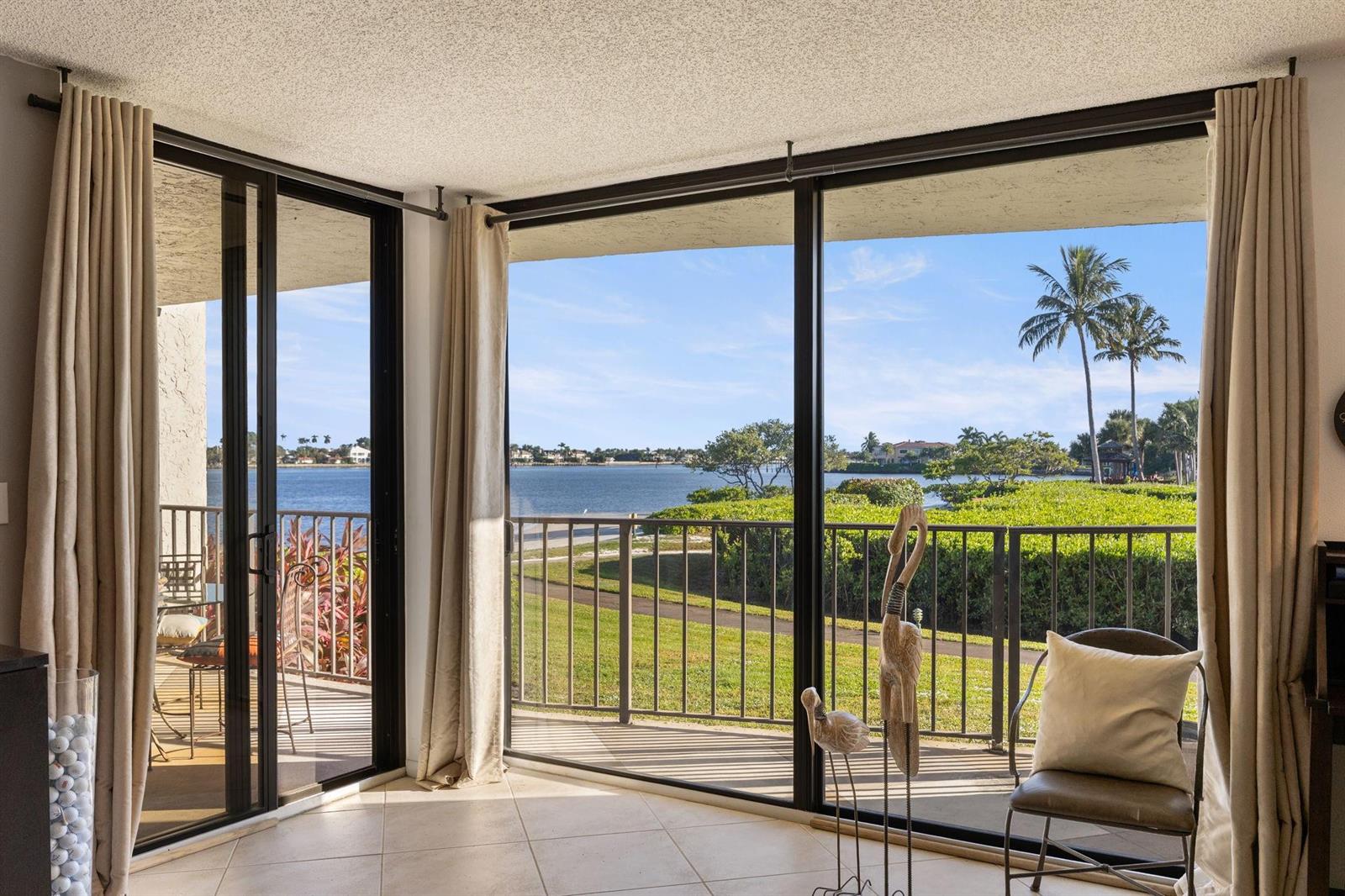 A room with tile floors and floor-to-ceiling windows overlooking a balcony, lawn, and water — 7020 Half Moon Circle # 105, Hypoluxo FL 33462, HYPOLUXO, FL