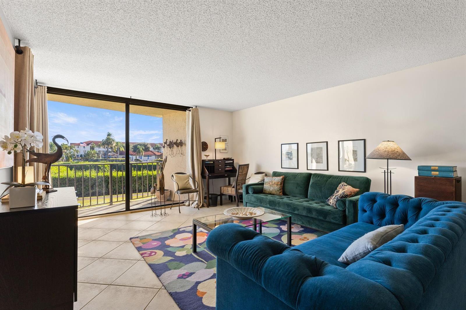 A living room features a blue tufted sofa, green velvet sofa, and a balcony view — 7020 Half Moon Circle # 105, Hypoluxo FL 33462, HYPOLUXO, FL