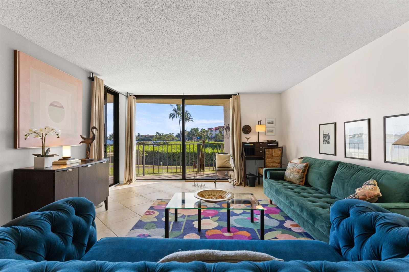 A living room features a blue sofa, a green sofa, a colorful rug, and a balcony — 7020 Half Moon Circle # 105, Hypoluxo FL 33462, HYPOLUXO, FL