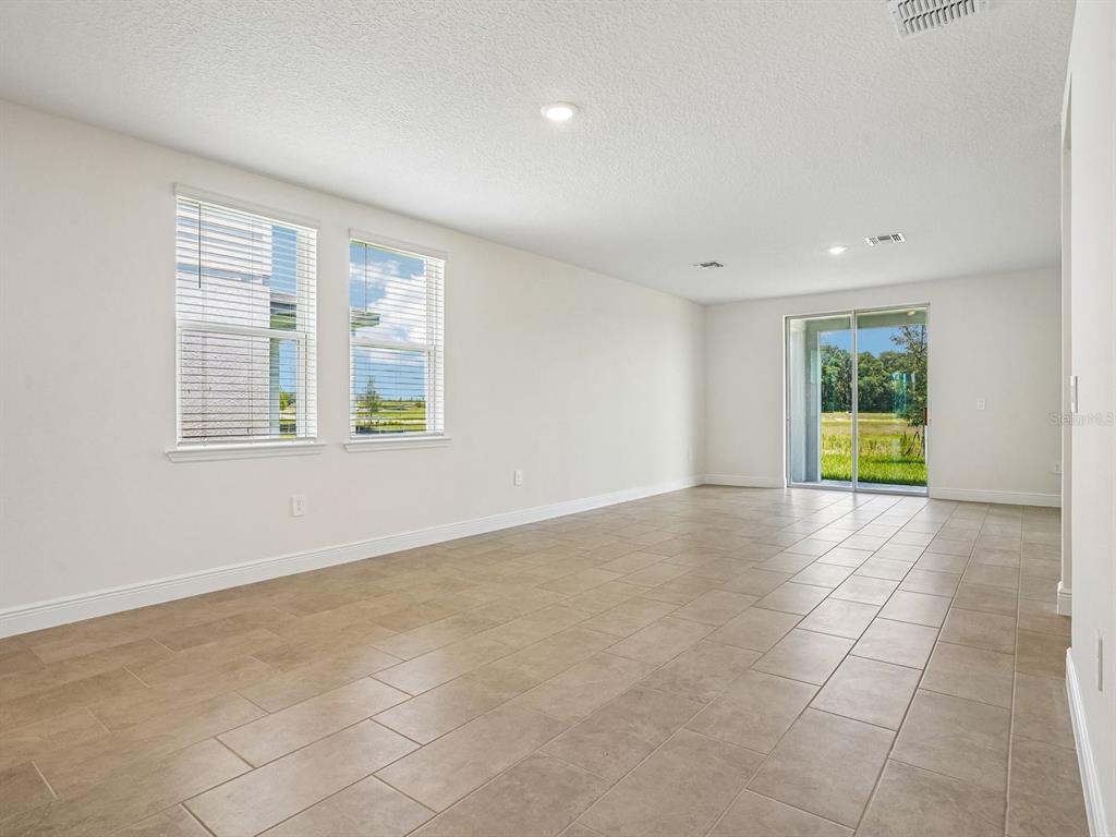 An empty room with beige tile flooring, white walls, two windows, and a sliding glass door — 3389 LINGER LANE, LAKE HAMILTON, FL
