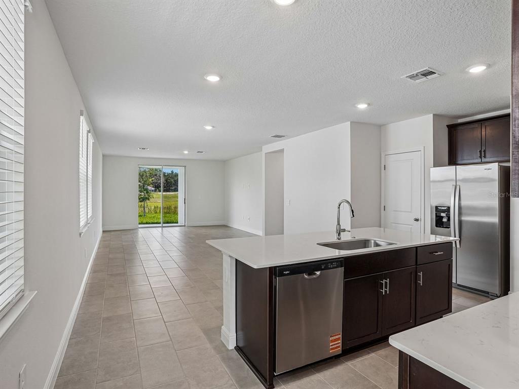 A kitchen with dark cabinets and stainless steel appliances overlooks an open-concept living area — 3389 LINGER LANE, LAKE HAMILTON, FL