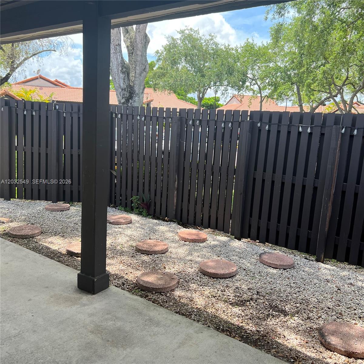 A patio features a dark wooden fence, gravel ground cover, and circular stone stepping stones — 15272 SW 46th Ln # 66, Miami FL 33185, MIAMI, FL