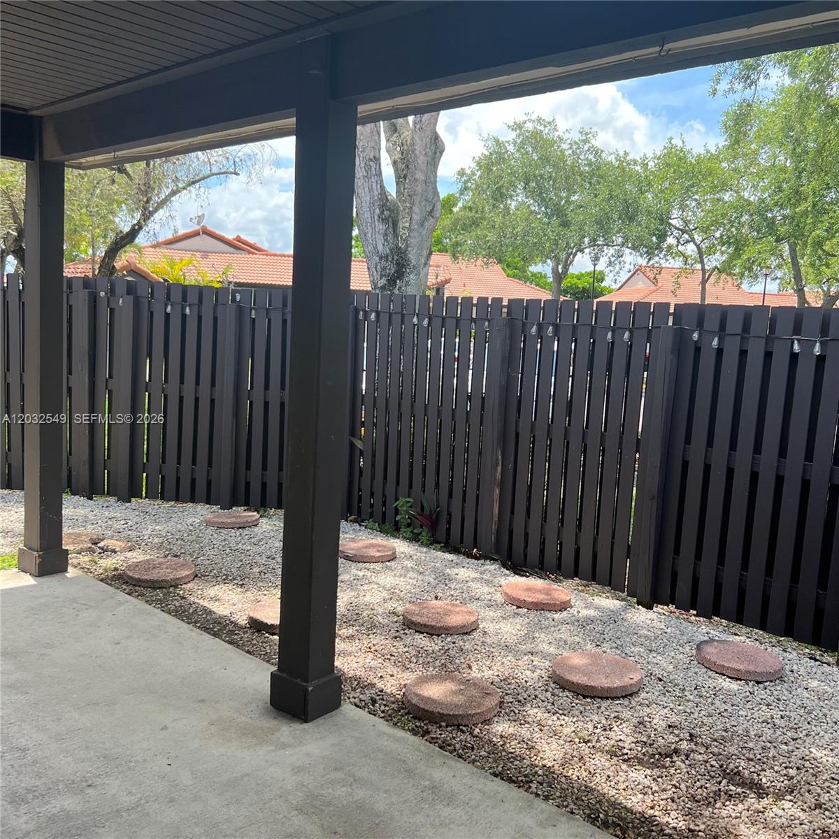 A covered patio features a gravel ground cover with round stepping stones and a wooden fence — 15272 SW 46th Ln # 66, Miami FL 33185, MIAMI, FL
