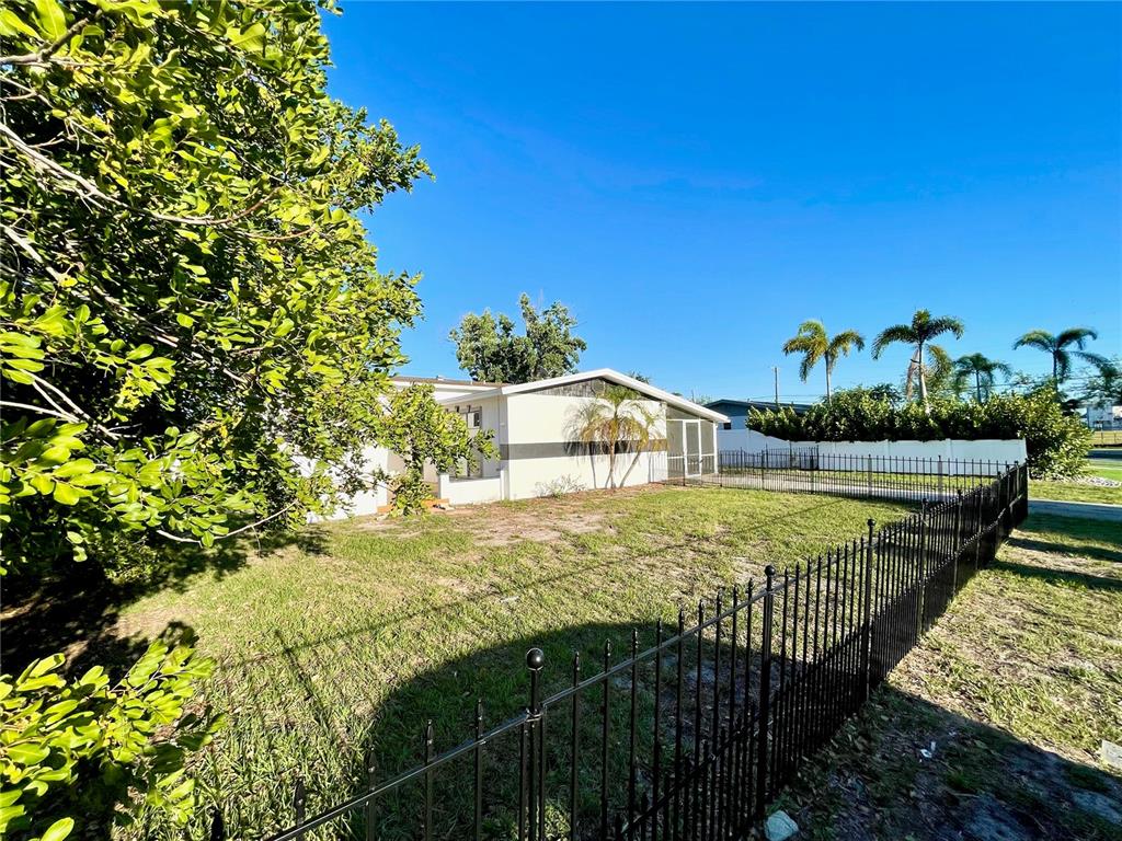 A fenced backyard features a white house with a screened porch and palm trees — 4608 S HESPERIDES STREET, TAMPA, FL