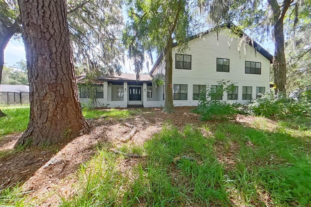 A two-story white house with a dark roof sits among large trees and grass — 6249 LAKE DRIVE, STARKE, FL