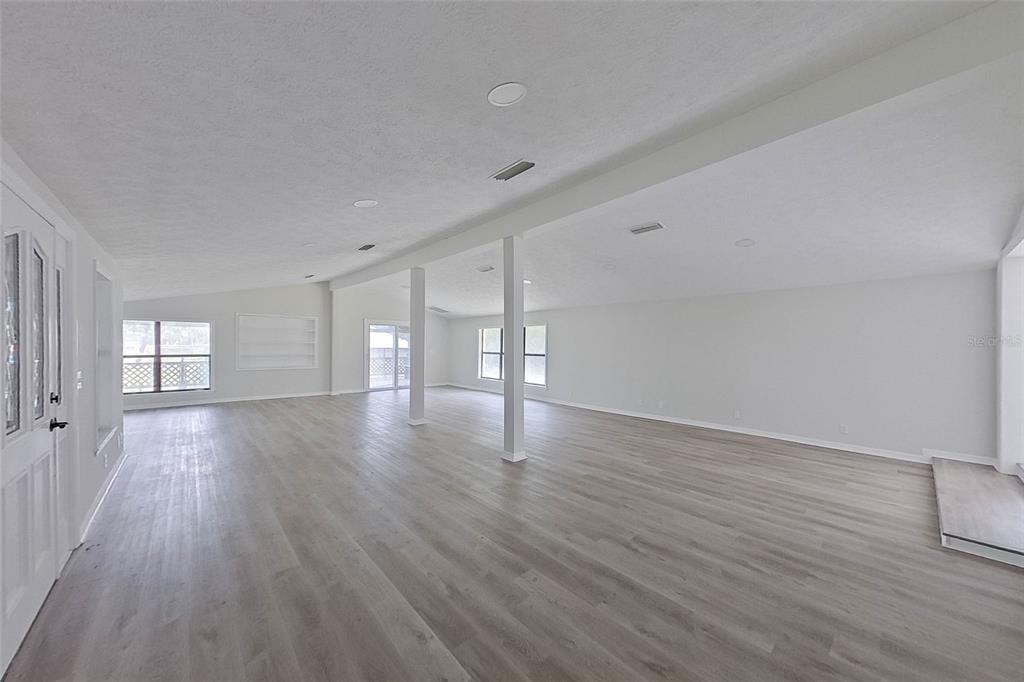 A spacious, open-concept living area features light gray wood-look flooring and white support columns — 6249 LAKE DRIVE, STARKE, FL