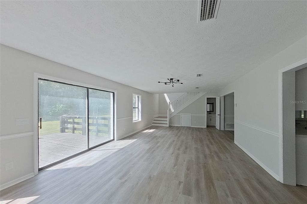 An open living area features light wood-look flooring, a sliding glass door, and a staircase — 6249 LAKE DRIVE, STARKE, FL
