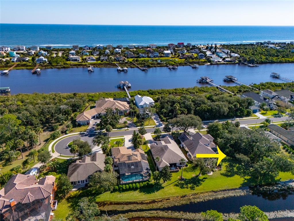 An aerial view shows a residential neighborhood with houses, a canal, and the ocean beyond — 63 N RIVERWALK DRIVE, PALM COAST, FL