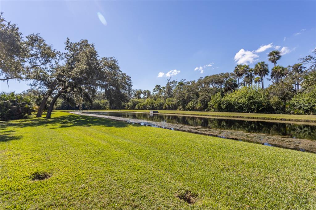 A grassy lawn slopes down to a long, narrow pond bordered by trees and palms — 63 N RIVERWALK DRIVE, PALM COAST, FL