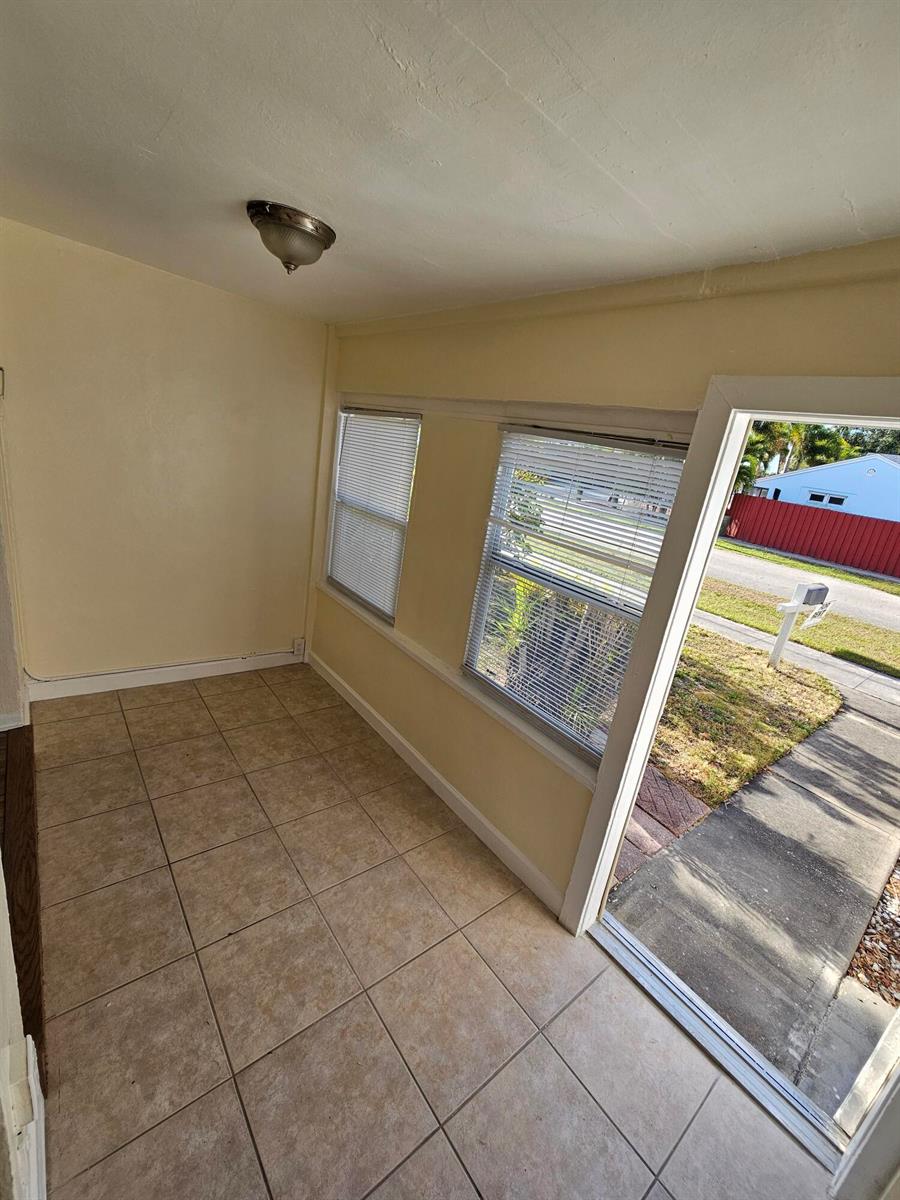 A sunroom with beige tile flooring, two windows with blinds, and a sliding glass door — 115 E Palm Street E # 117, Lantana FL 33462, LANTANA, FL