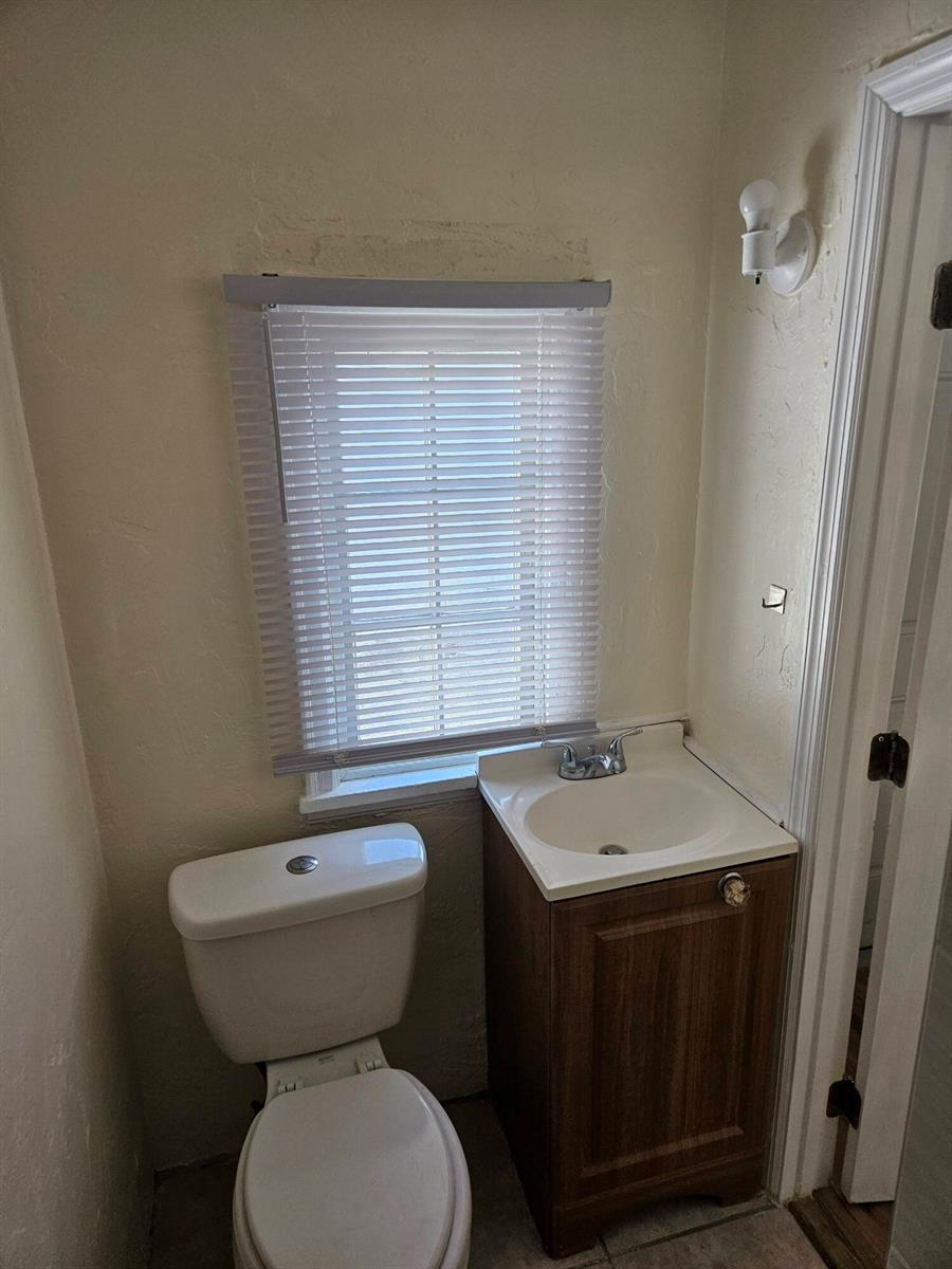 A small bathroom features a white toilet, a wood vanity with a sink, and a window — 115 E Palm Street E # 117, Lantana FL 33462, LANTANA, FL