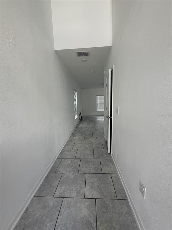 A long hallway with gray tile flooring leads toward a room with two windows — 598 BELL PRAIRIE CIRCLE, LAKE WALES, FL
