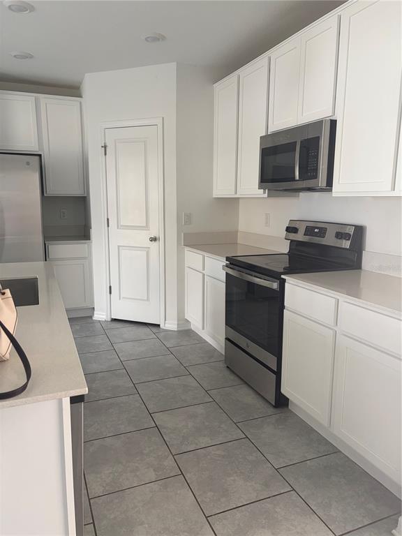 A kitchen features white cabinets, stainless steel appliances, quartz countertops, and gray tile flooring — 598 BELL PRAIRIE CIRCLE, LAKE WALES, FL