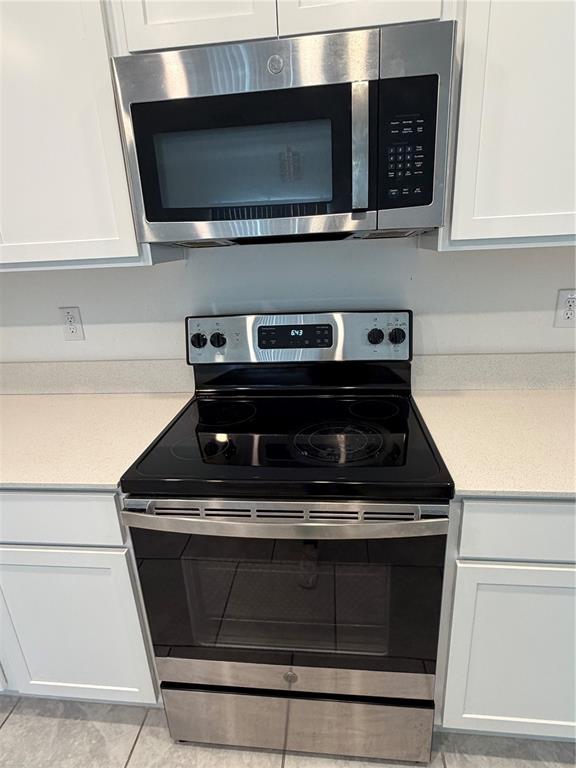 A stainless steel microwave and electric range are installed between white kitchen cabinets — 598 BELL PRAIRIE CIRCLE, LAKE WALES, FL
