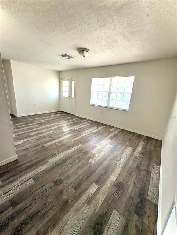 An empty room features wood-look vinyl flooring, white walls, a ceiling light, and a window — 8151 HIXTON DRIVE, PORT RICHEY, FL