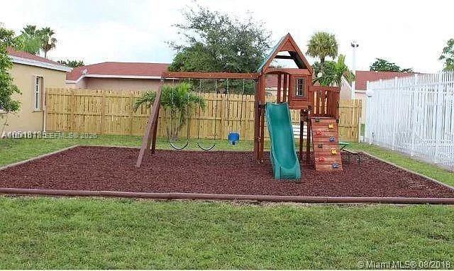 A wooden playset with a slide and swings sits on a mulched area in a backyard — 885 NE 213th Ter # 2, Miami FL 33179, MIAMI, FL