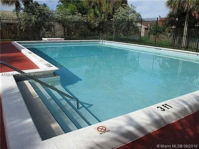 An outdoor rectangular swimming pool with steps and a metal railing is surrounded by fencing — 885 NE 213th Ter # 2, Miami FL 33179, MIAMI, FL