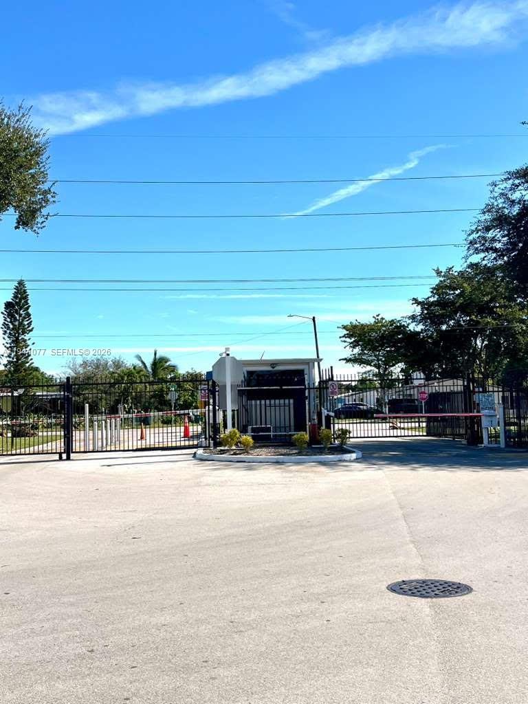 A gated entrance with a security booth and metal fencing under a clear blue sky — 885 NE 213th Ter # 2, Miami FL 33179, MIAMI, FL